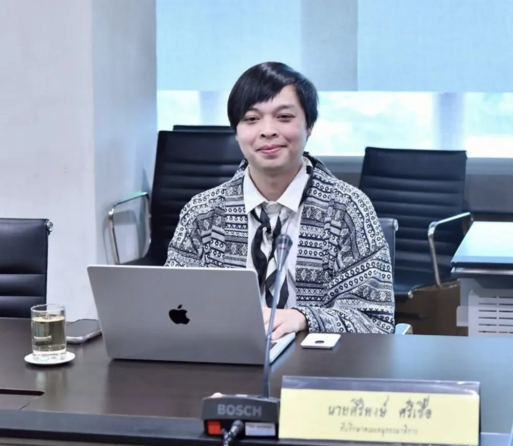 Arm seated at a Thai parliamentary subcommittee meeting with a laptop and name plate
